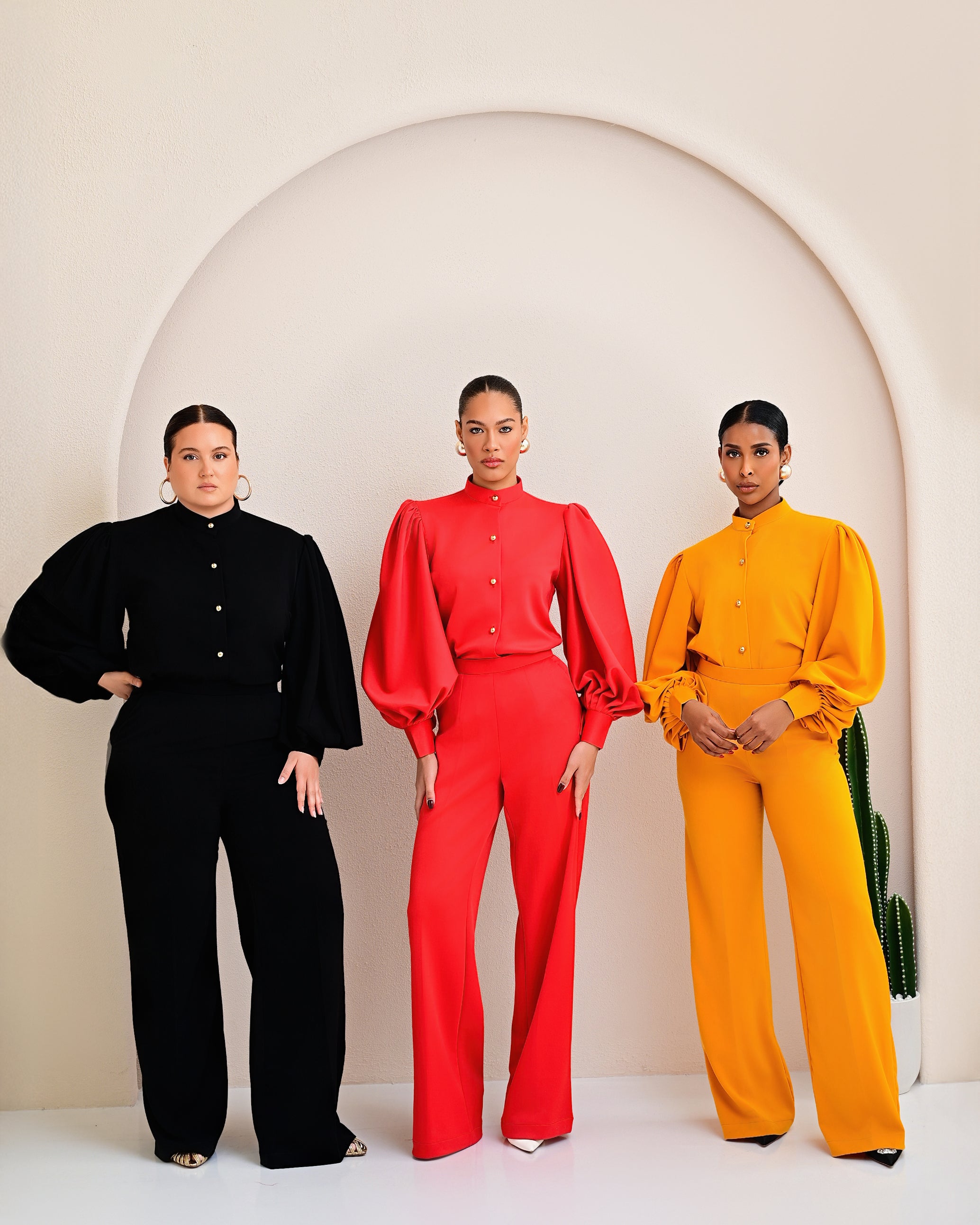 Three women in black, red, and yellow outfits standing against a white background with an arch.