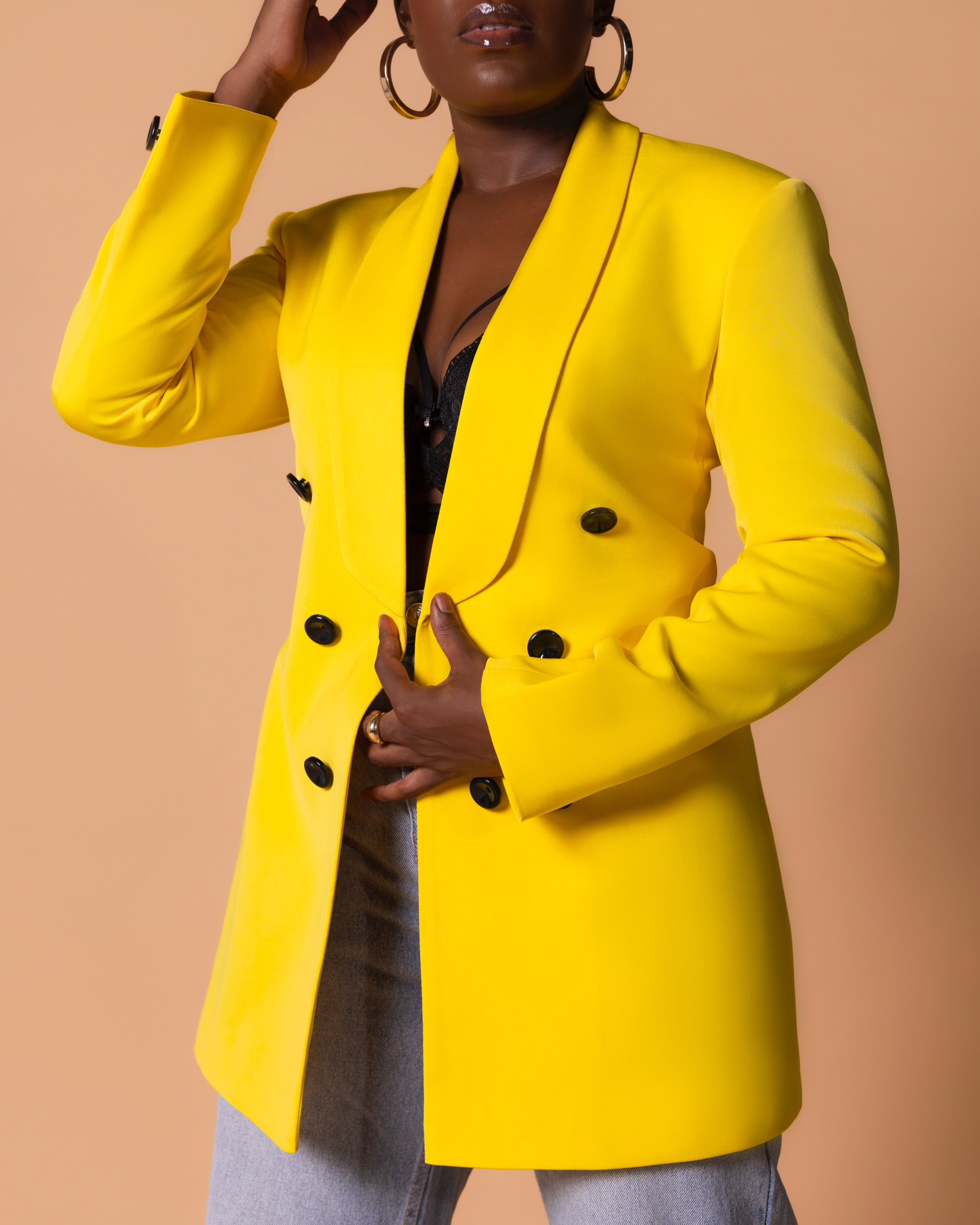 Model wearing yellow structured blazer with black button accents, styled casually with denim and a black, sophisticated bralet.