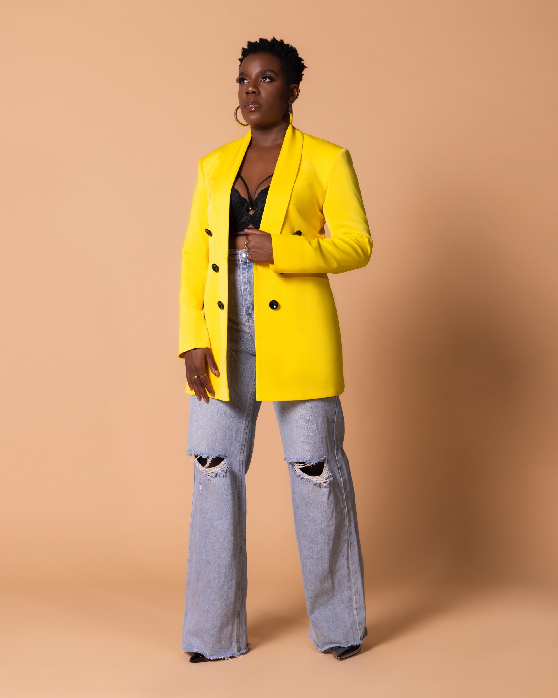 Model wearing yellow structured blazer with black button accents, styled casually with denim and a black, sophisticated bralet.