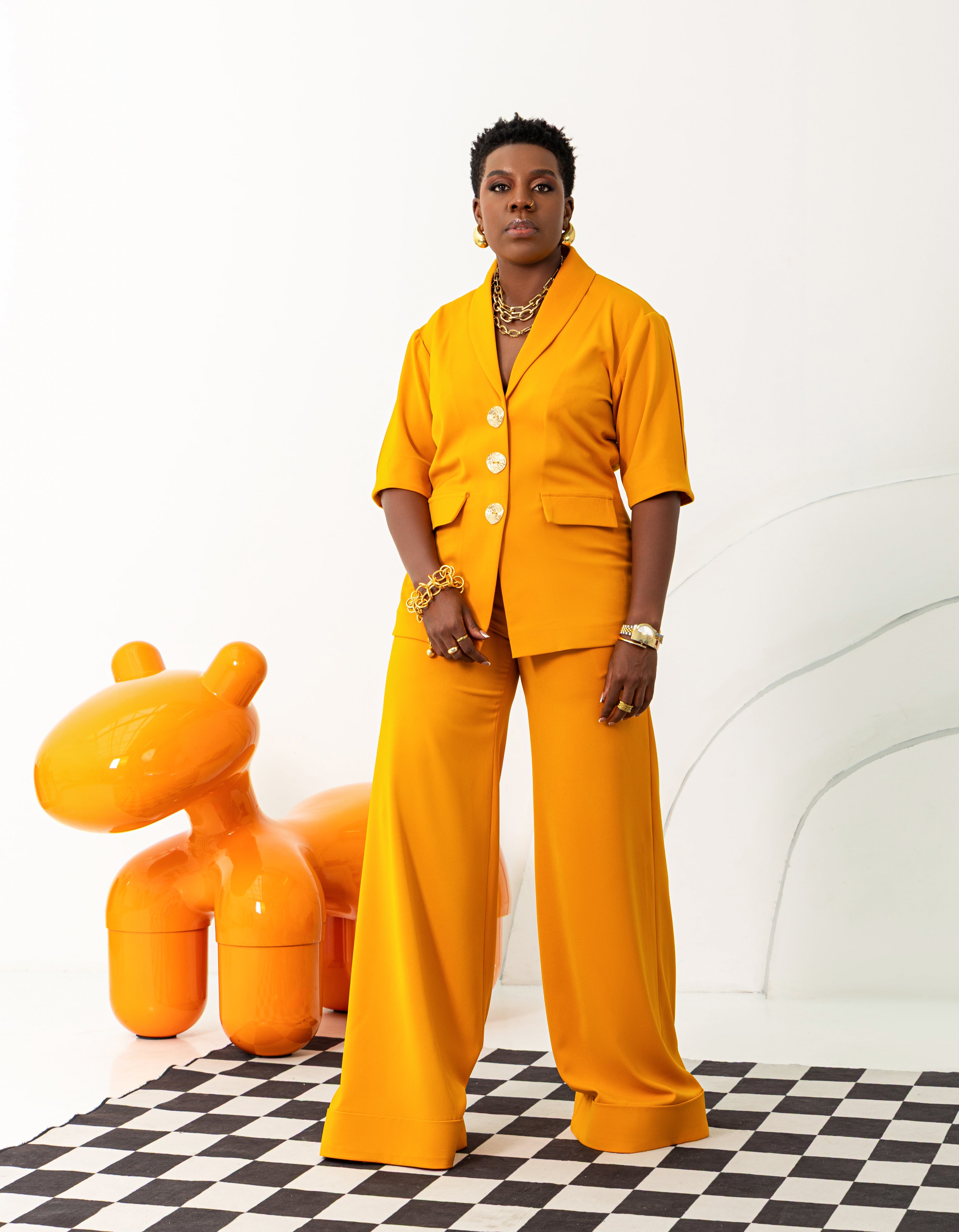 An elegant looking woman wearing mustard yellow co-ord set featuring a short sleeve top with gold buttons, and wide-leg trousers with turn-up hems. 