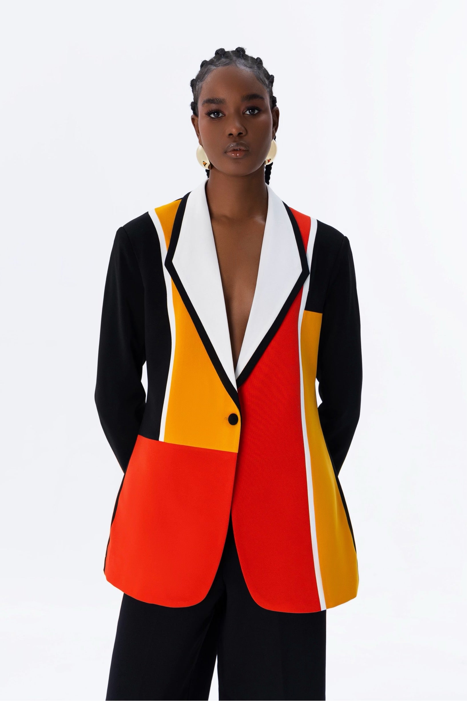 A model wearing a color block long sleeve blazer with a lapel collar and single button closure. The blazer has red, black, and mustard yellow panels.