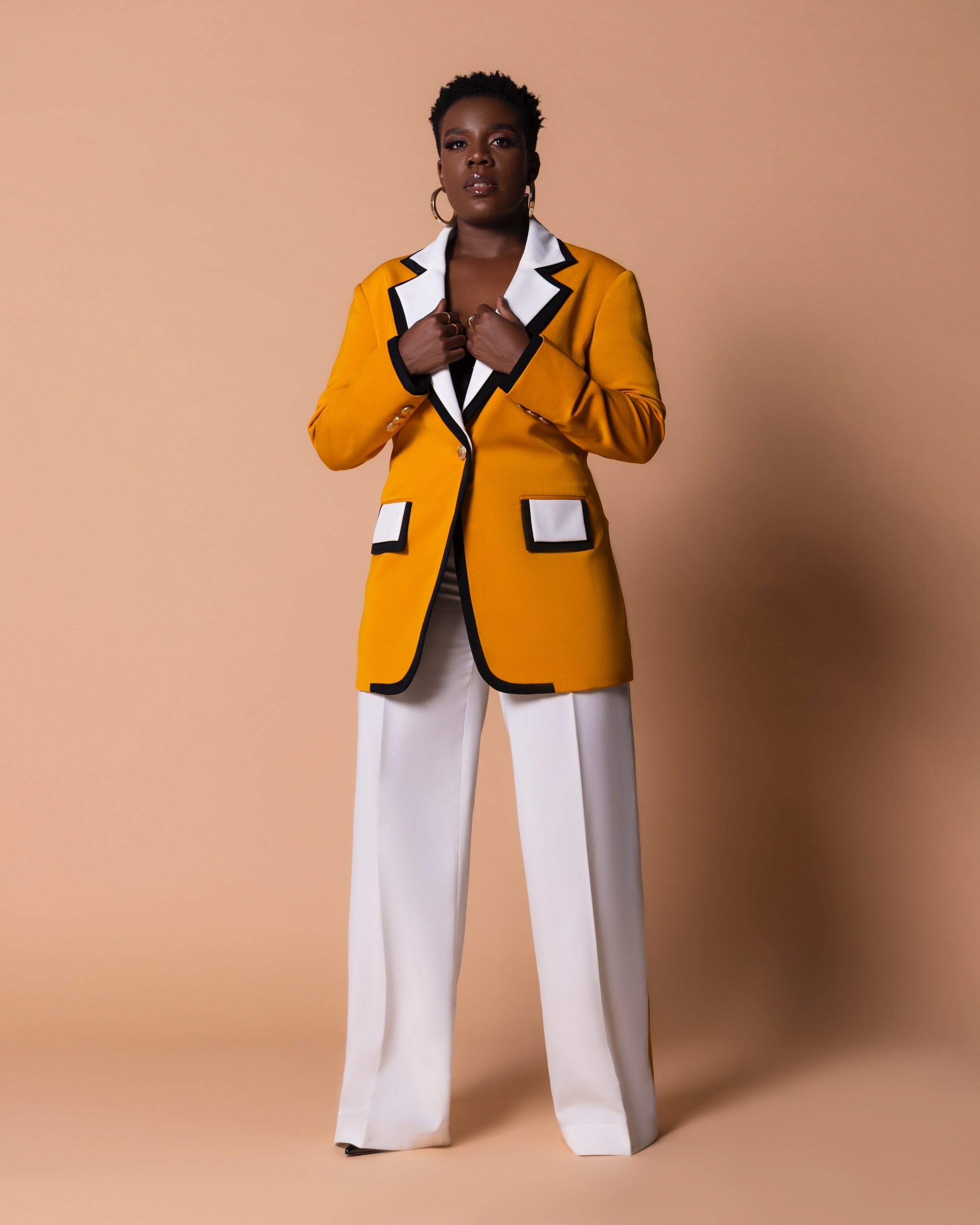 Woman wearing mustard yellow blazer with a straight white, high-waist pants featuring black and mustard stripes on the sides for a flawless elegant look.