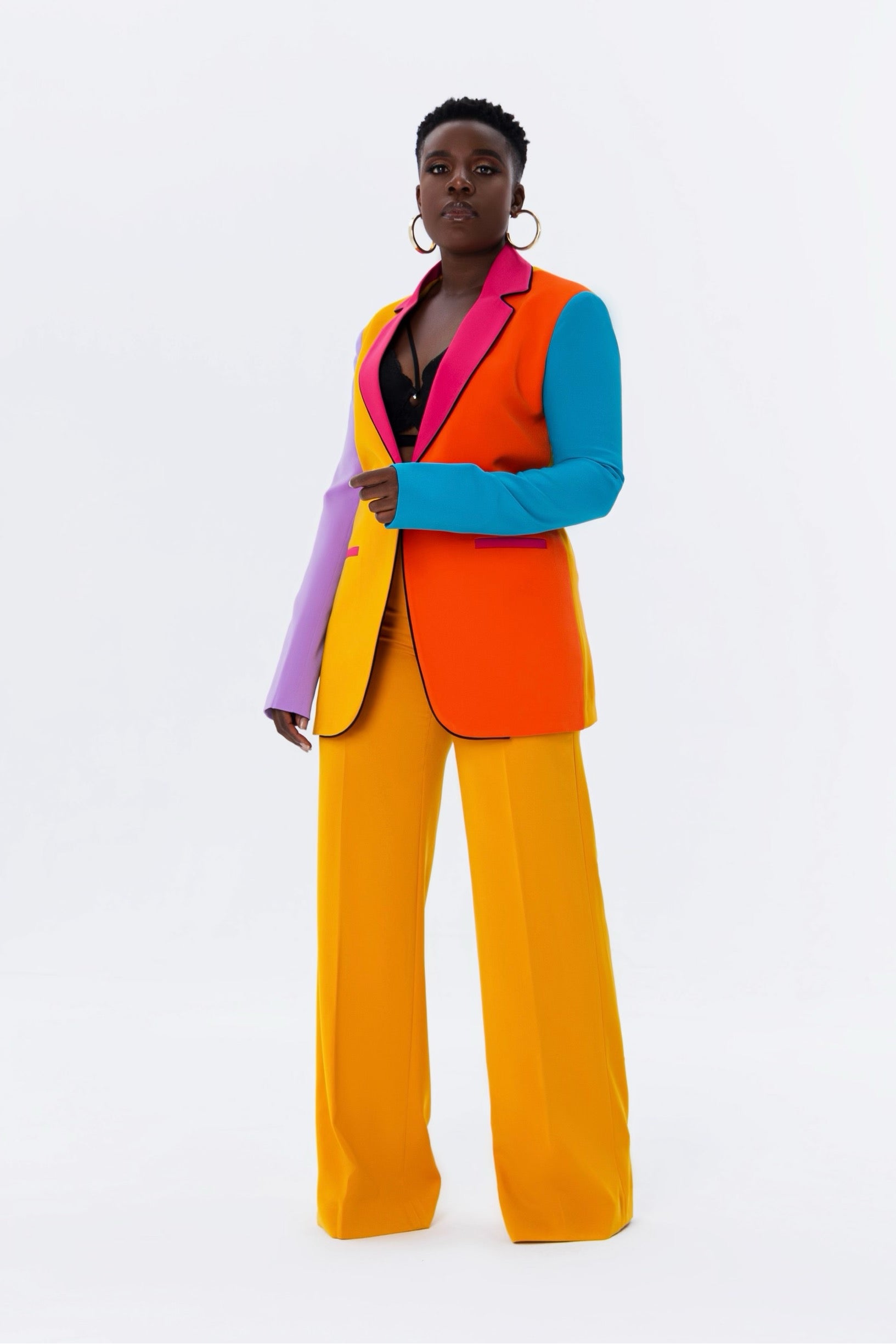 Front view of woman wearing multi colored tailored blazer with colorblock sleeves in lilac, turquoise, pink, mustard yellow, and orange.