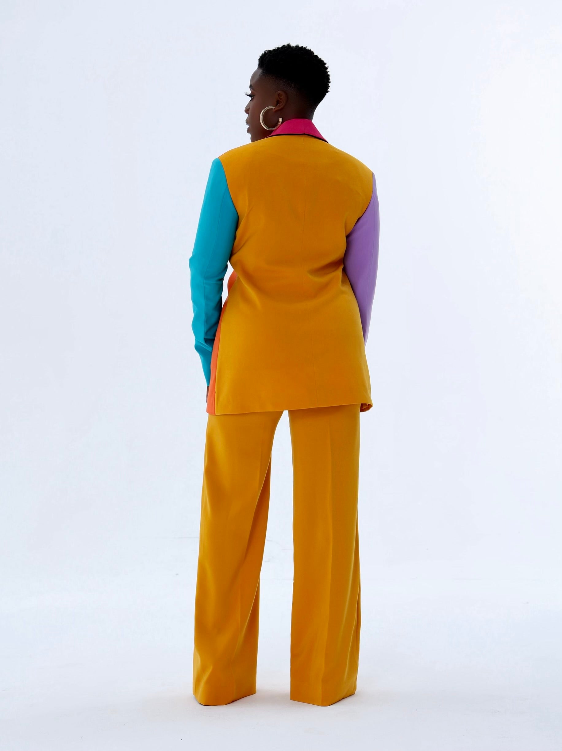 Back view of multicolored tailored blazer with vibrant colorblock design in orange, mustard yellow, pink, lilac, and turquoise sleeves