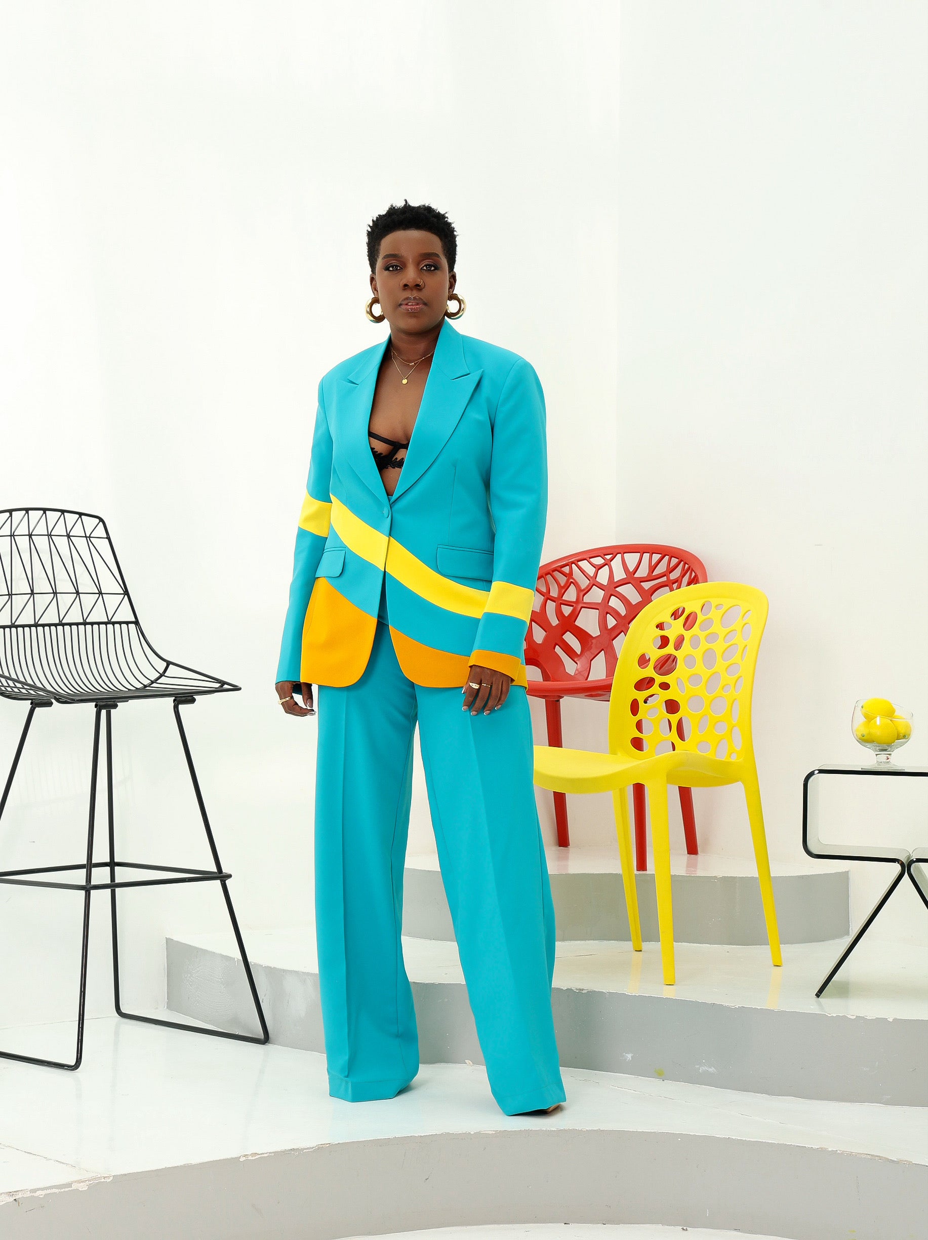 Woman wearing teal blazer with yellow and mustard diagonal colorblock design, paired with a high-waist straight pants. 