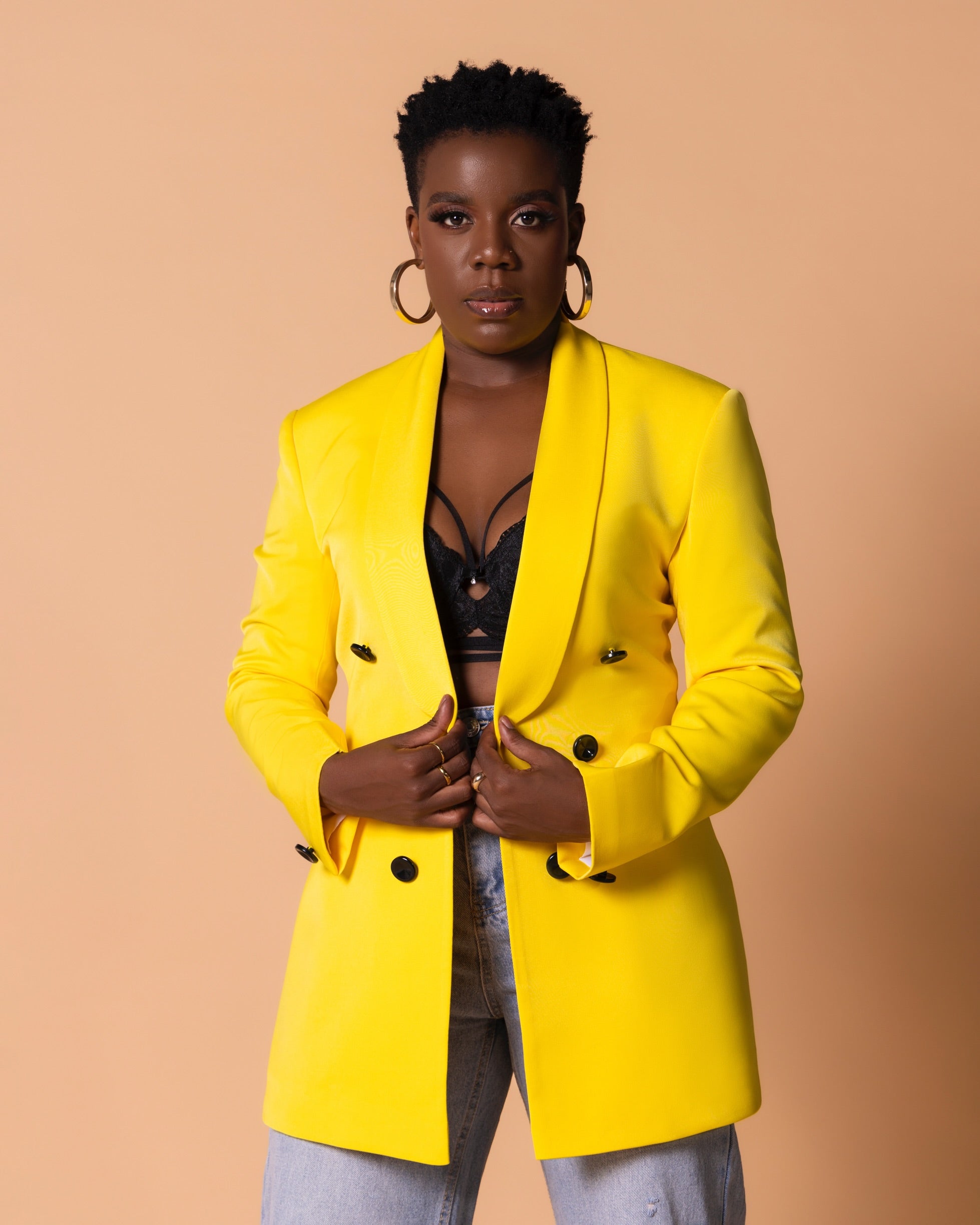 Woman in bright yellow double-breasted blazer with black buttons and lapel collar, styled over denim.