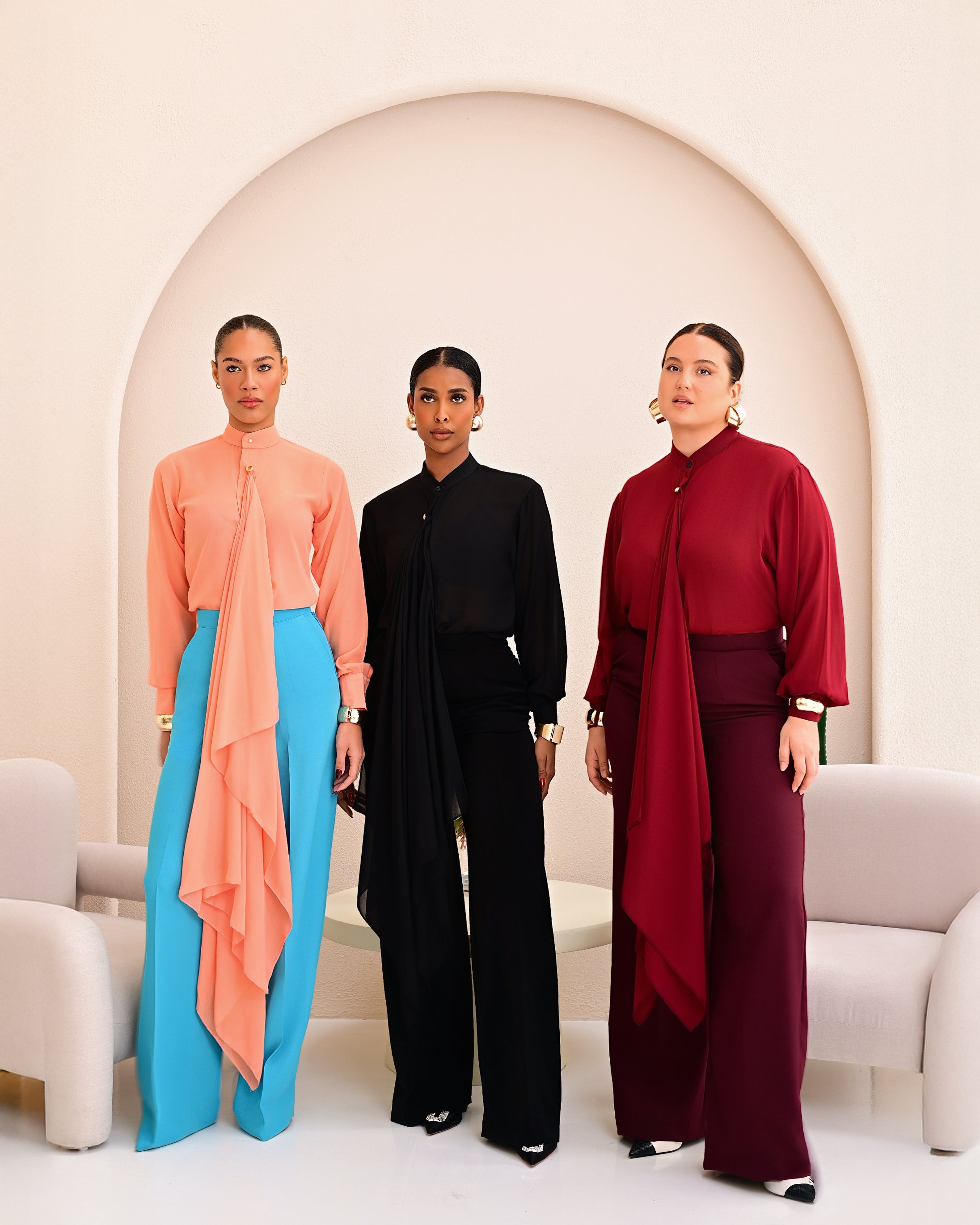 Three models wearing different variations of the elegant Tabitha co-ord set from Olarsgrace – Peach, Black and Wine.  The wine Tabitha features a chiffon drape blouse and matching tailored straight-leg pants.