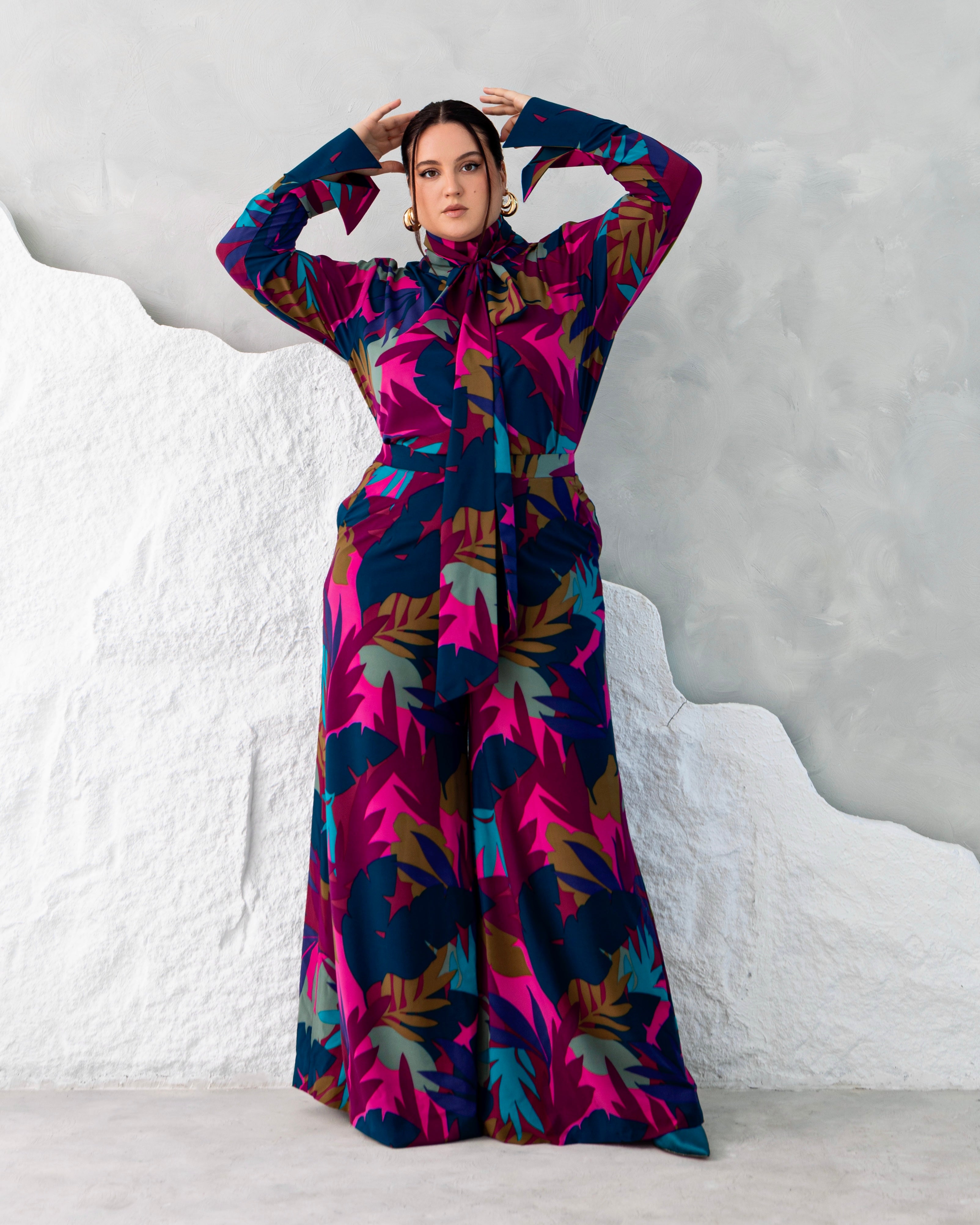 Model is wearing a luxe printed two-piece set featuring high-neck tie blouse and matching wide-leg crepe trousers.