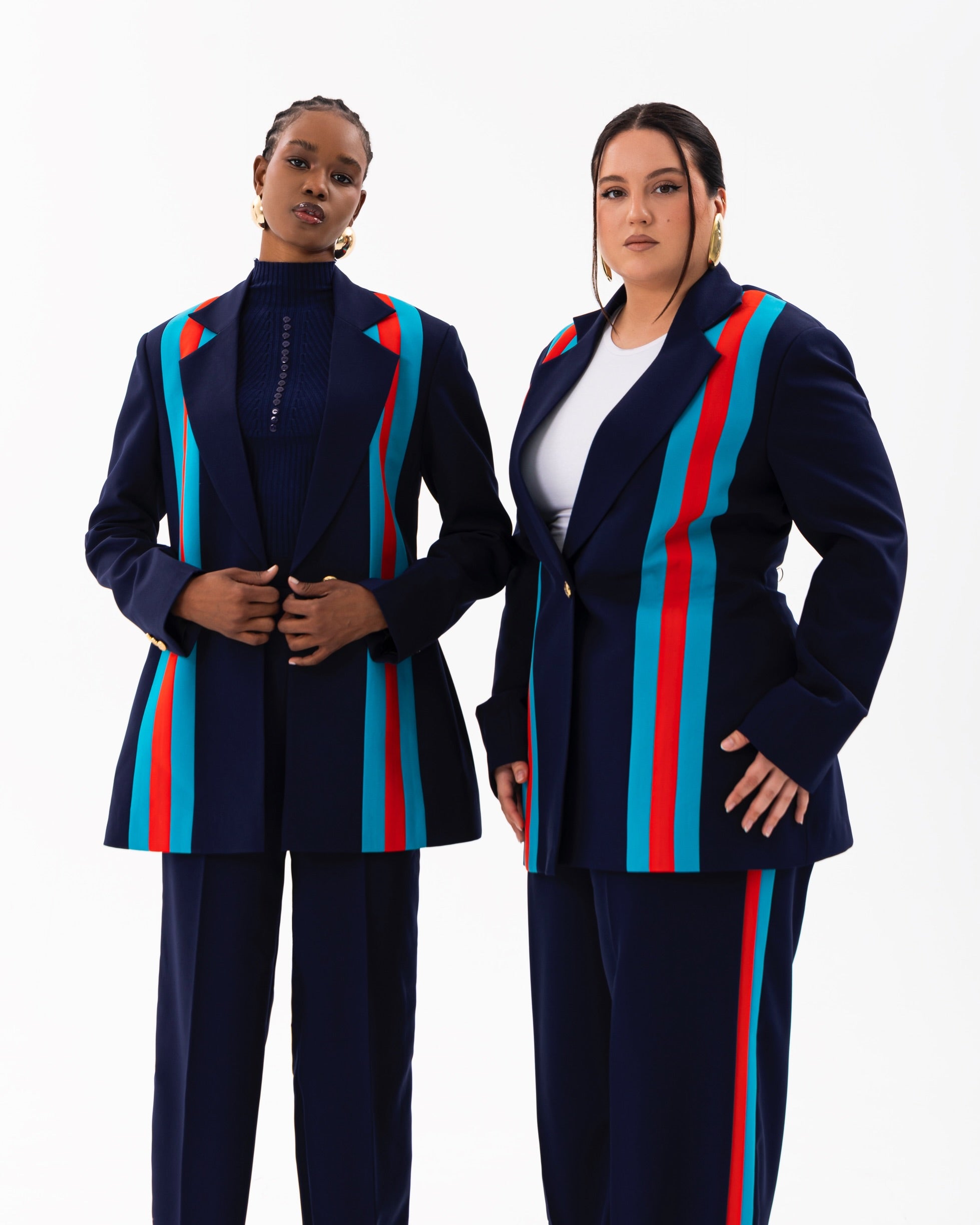 Two models wear the Fallon navy blue suit set featuring tailored blazers, with vertical teal and orange stripe accents,  and straight high-waist pants styled for diverse body type. 