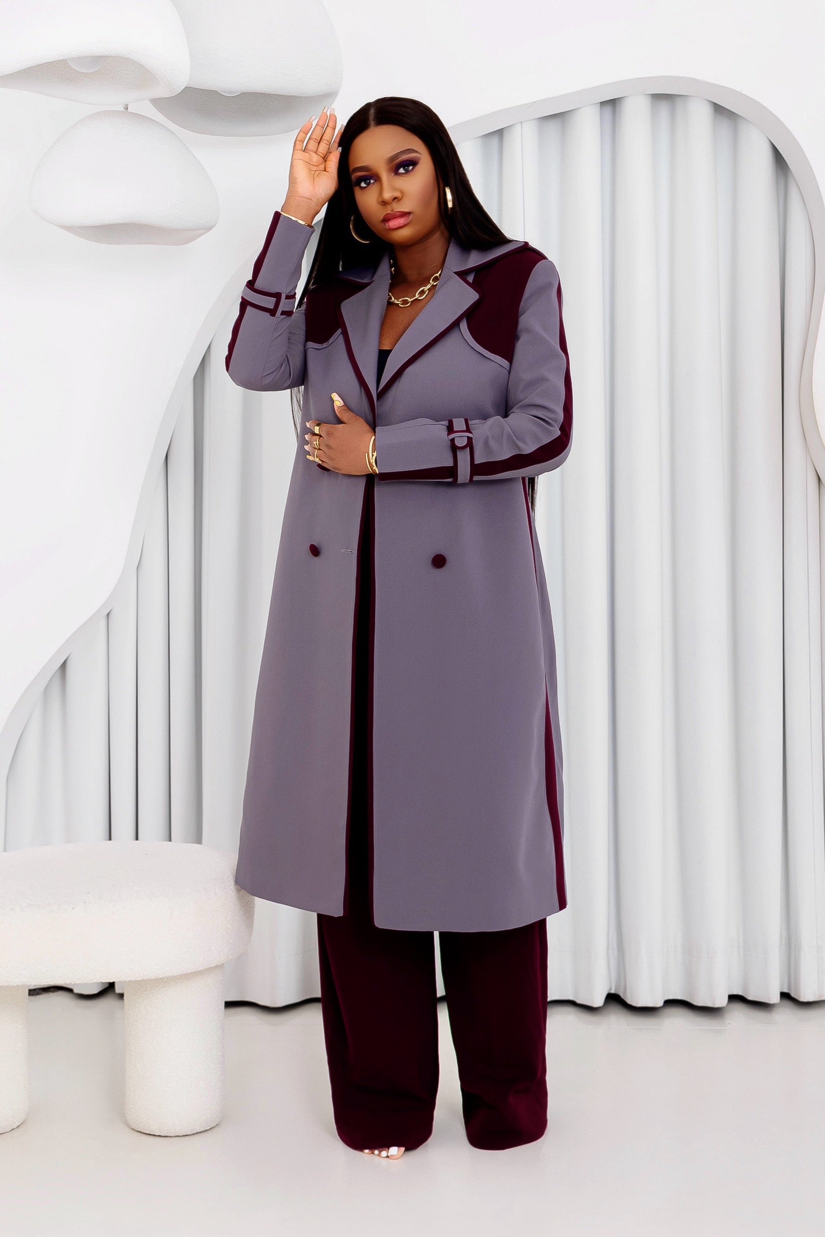 Side view of a model in the Grace Trench Coat, showcasing aubergine sleeve piping and tailored structure, styled with matching pants.