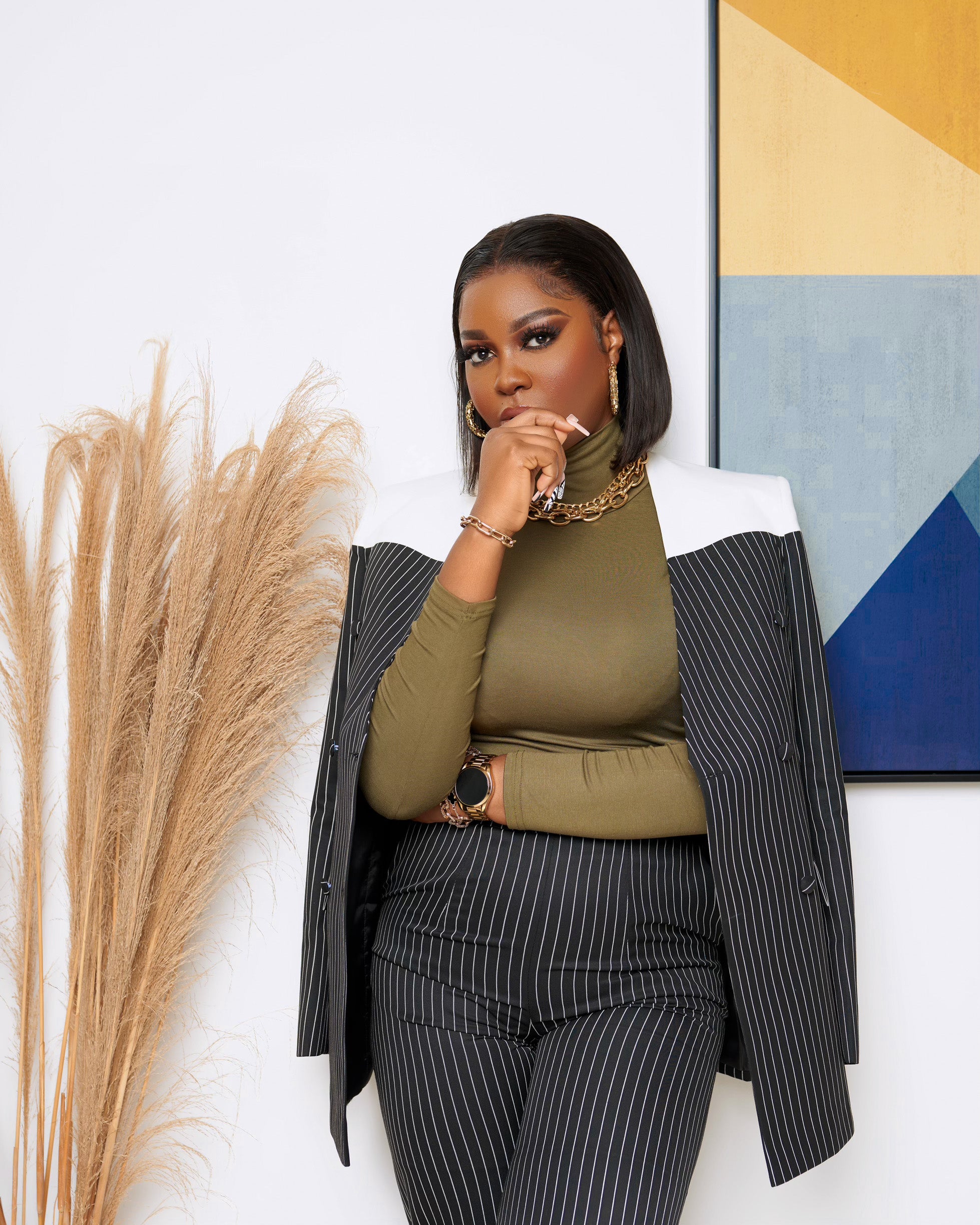 Woman wearing a tailored black and white pinstripe suit set, featuring a longline blazer with white shoulder detail and straight-leg trousers