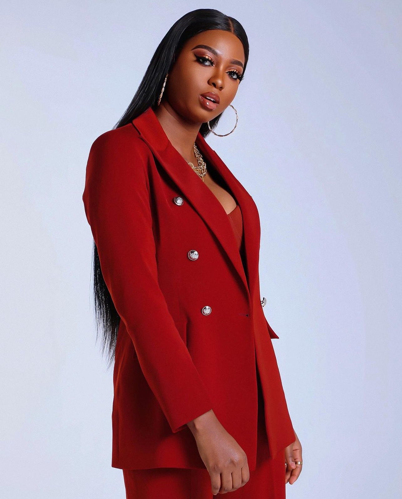 Model wearing Mitra burgundy suit set with double-breasted blazer, silver buttons and matching high-waist straight pants.