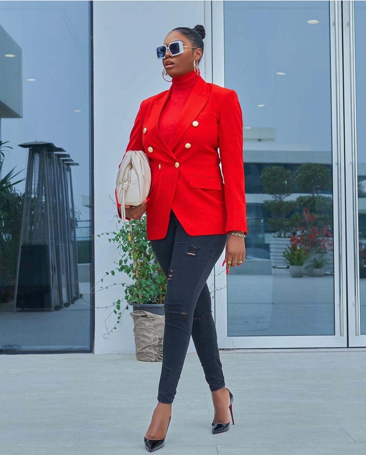 Model wearing a stylish red double-breasted blazer with gold buttons, paired with black jeans and heels.