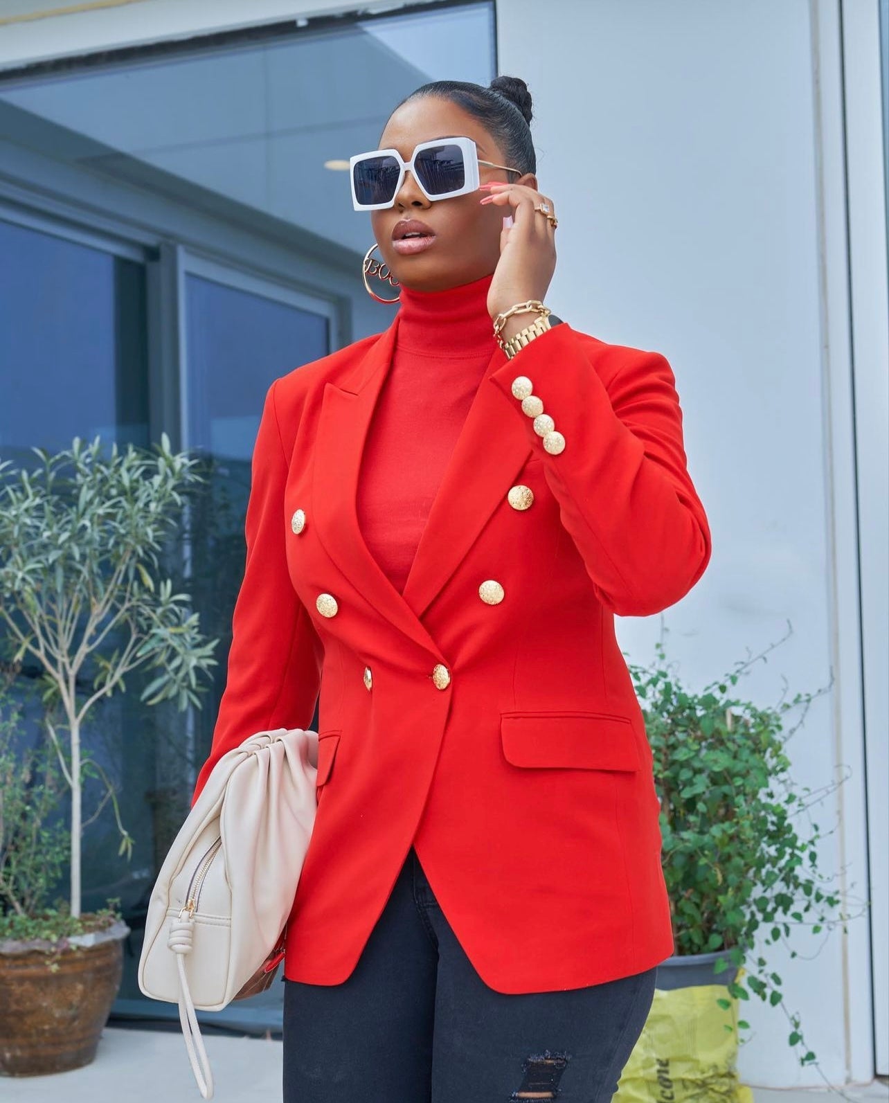 Close up view of model wearing a stylish red blazer paired with ripped black jeans and oversized sunglasses.