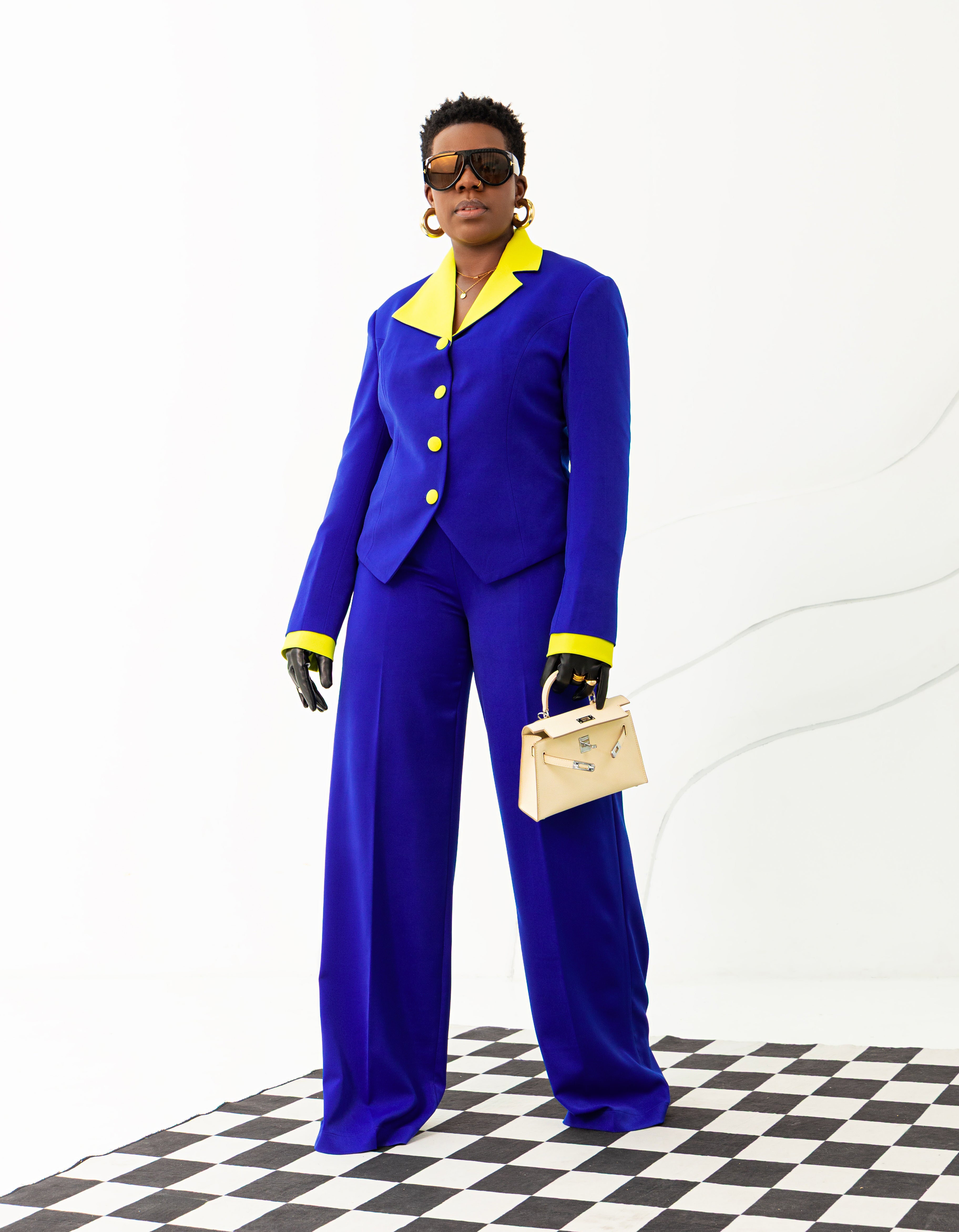 Model in royal blue suit set with neon green lapel, cuffs, and buttons, styled with wide-leg pants.