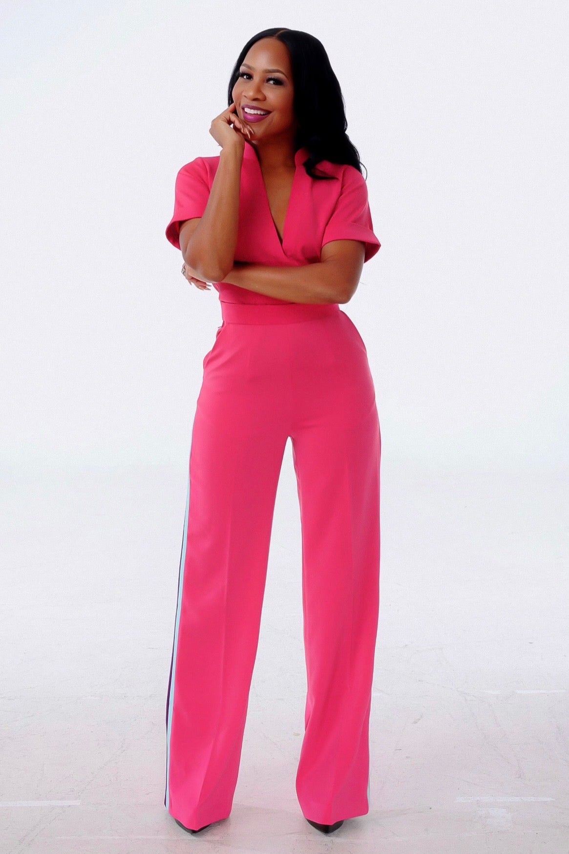 Model wearing pink pant set with deep V-neck short-sleeve top and straight-leg trousers with side stripe detail, studio full-length front view.