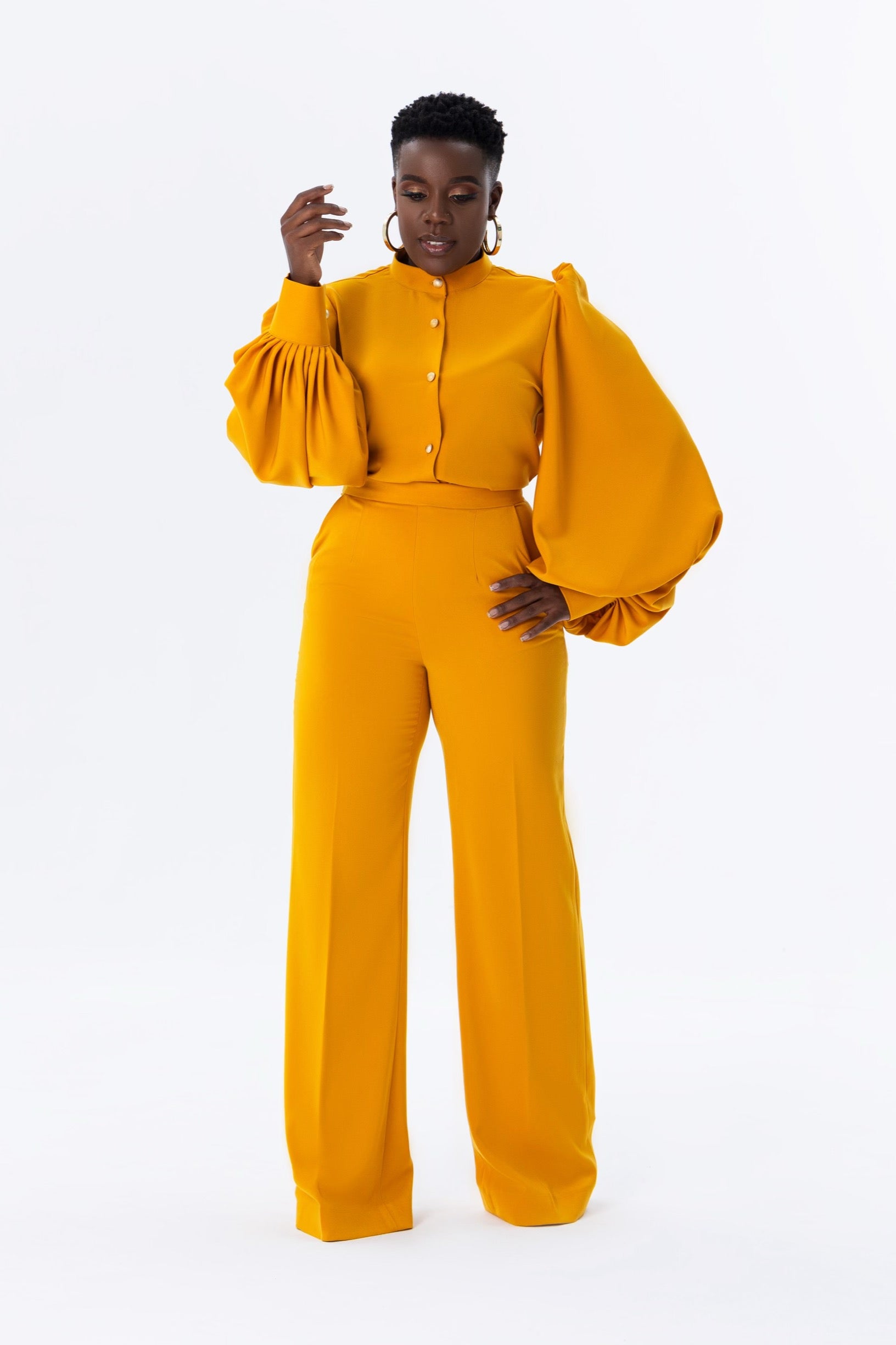 Model wearing Shabir mustard yellow set with bishop collar, gold buttons and exaggerated balloon sleeves, paired with matching high-waisted straight pants with pockets.