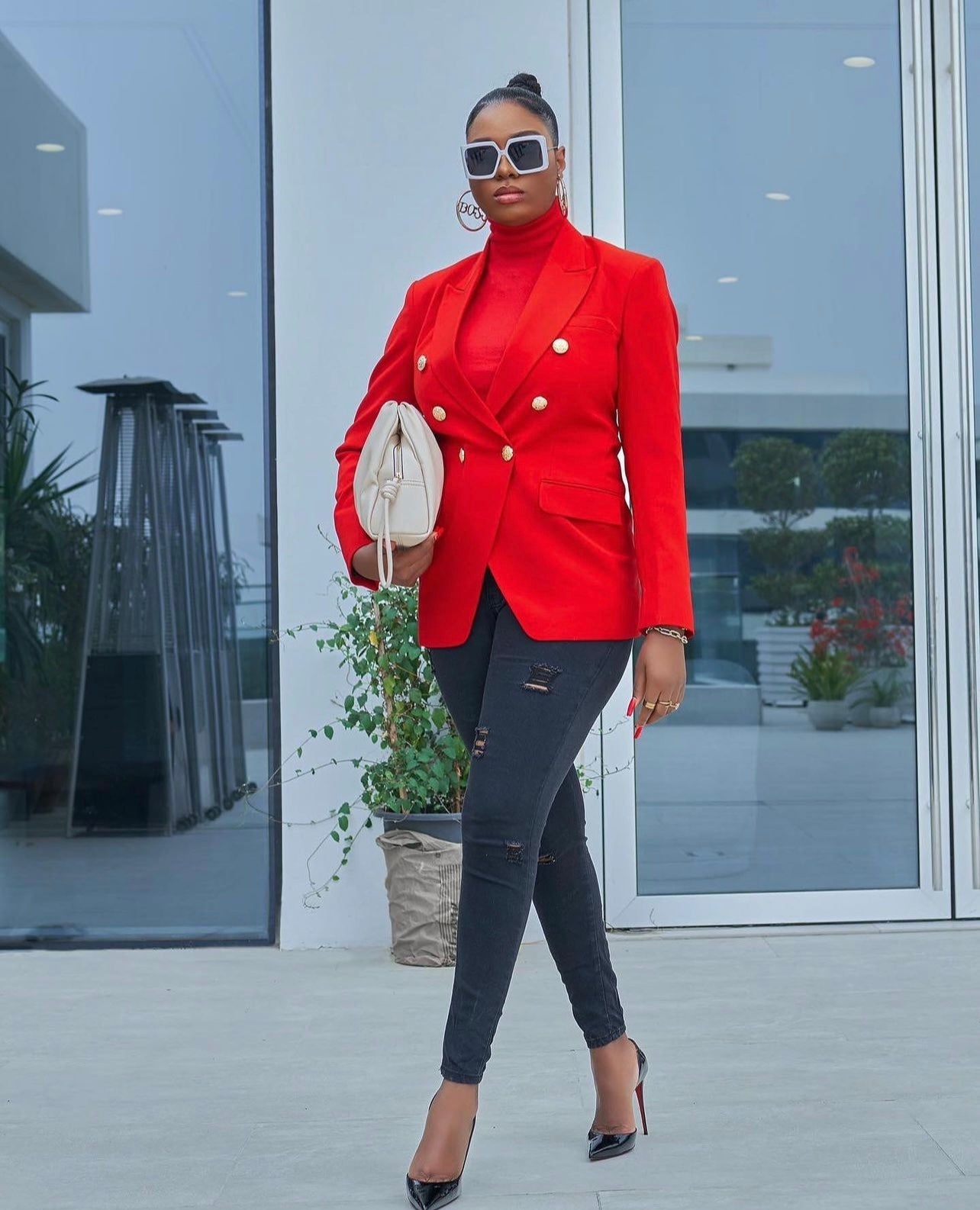 Model wearing a red double-breasted blazer with gold buttons, paired with black jeans and christian louboutin heels.