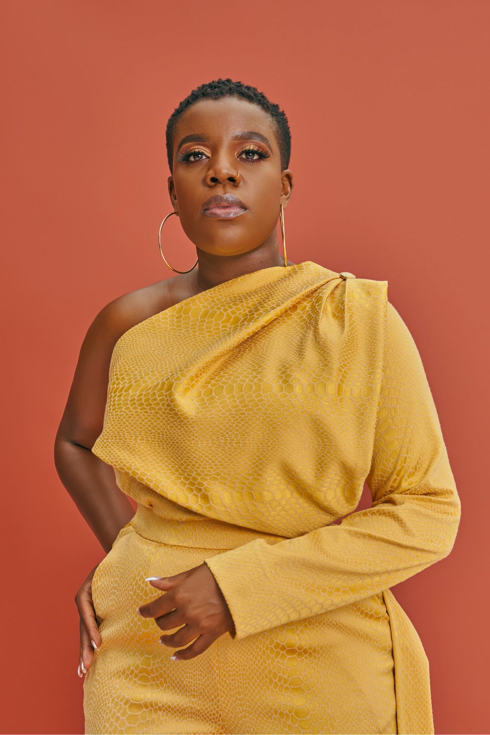 Close up view of the Neka Co-ord set in goldish yellow brocade. Showing mono-strap neckline, long sleeve, and extended side flap on high-waist pants.