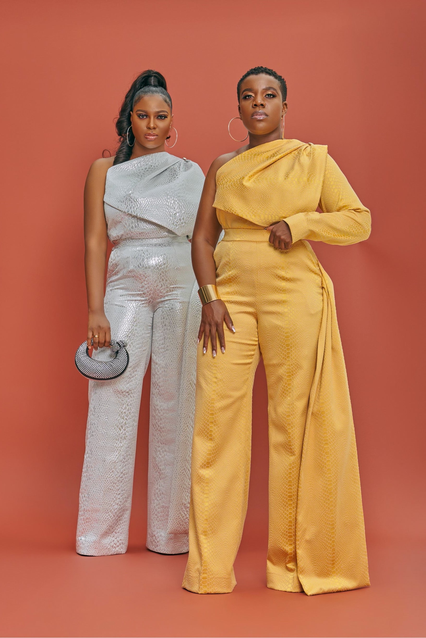 Two models wearing coordinating yellow and silver outfit sets, one in gold-yellow high-waisted pants with a flap on the side, and the other in silver mono-strap top with silver button detailing.