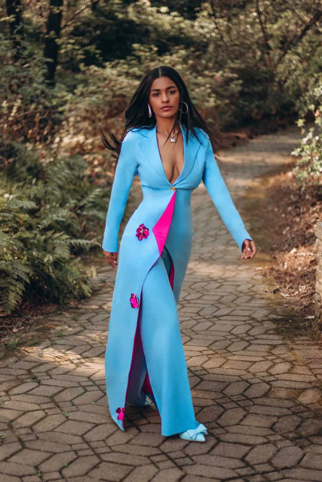Model wearing a long sky blue power suit set with hot pink contrast lining, and beaded appliqués, paired with high-waist straight-leg trousers.
