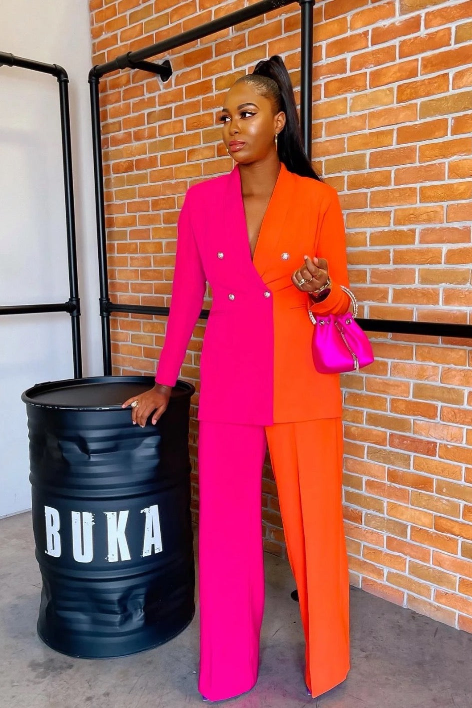 Woman wearing orange and pink symmetric colorblock women’s suit set, with long sleeve blazer and matching straight, high-waist pants.