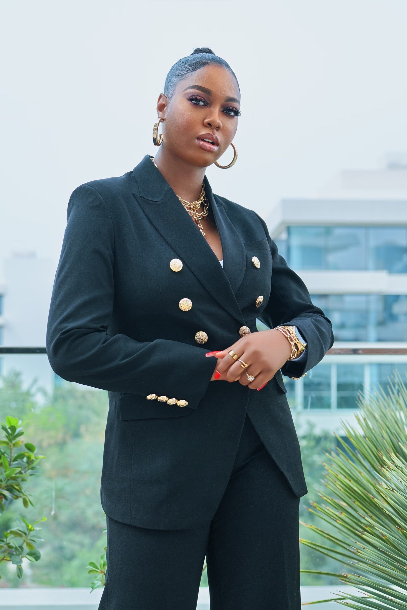 Model wearing a black double-breasted blazer with gold buttons, standing confidently outdoors.