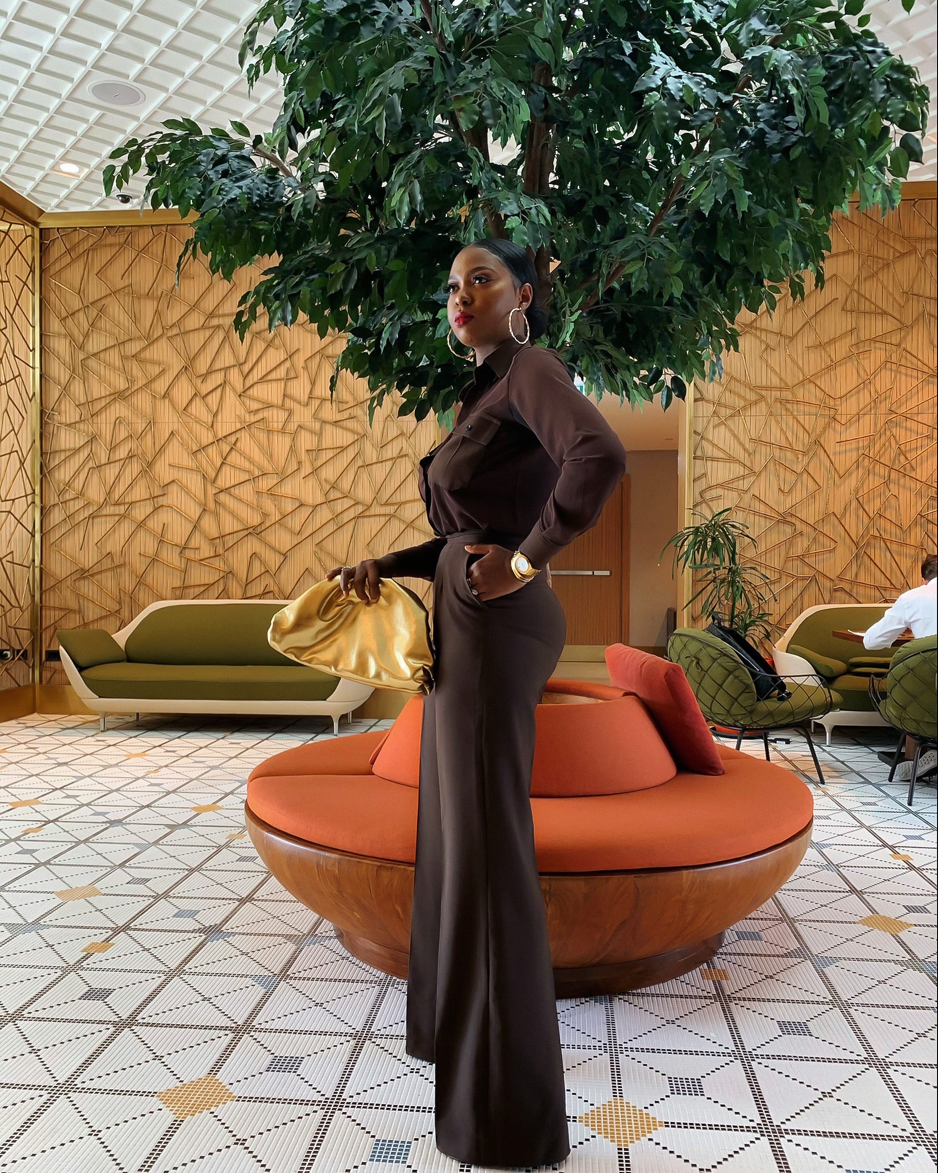 Model wearing Brown 21 Set in coffee brown featuring chiffon button-up shirt with double flap pockets and matching high-waist pants, side view.