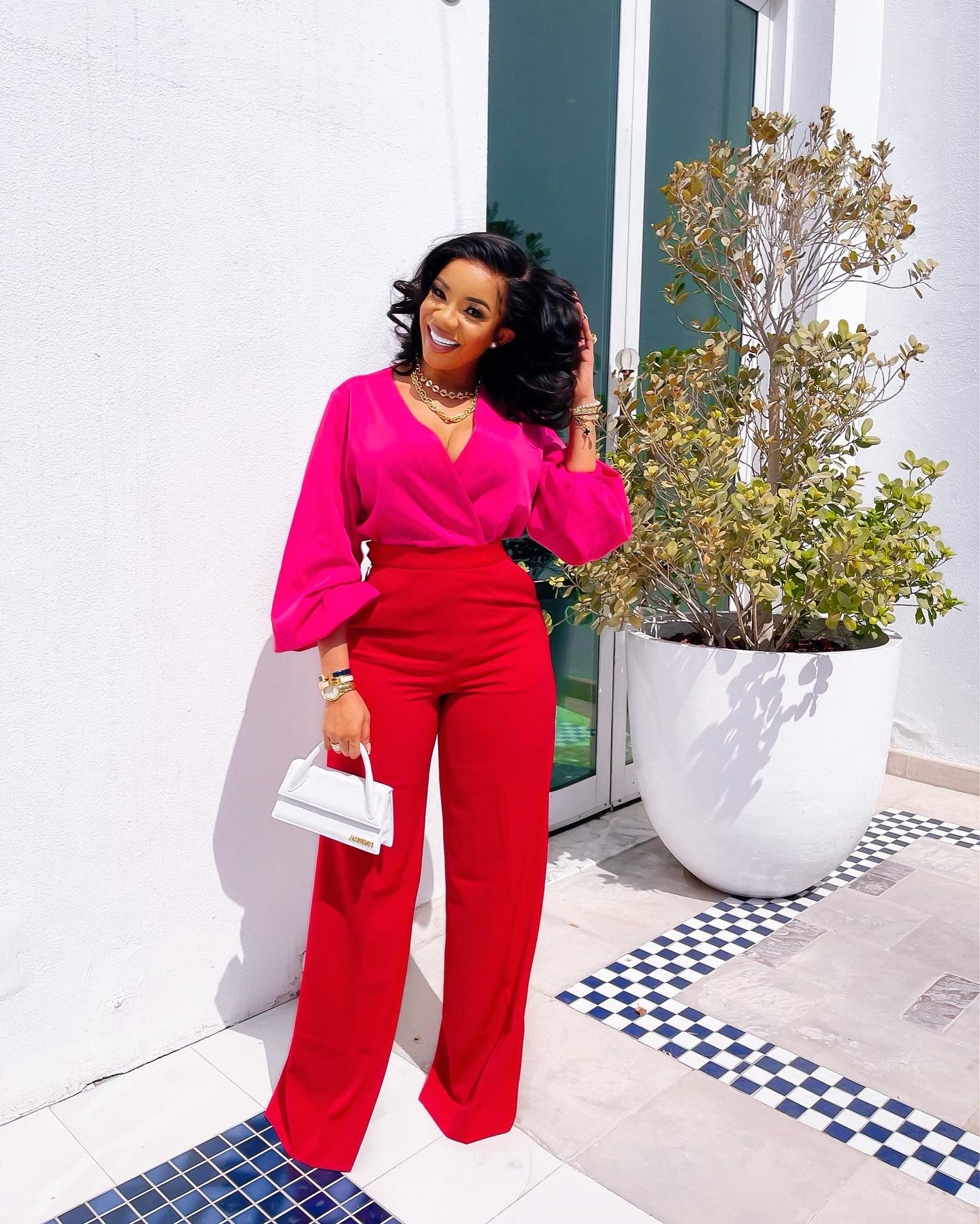 A woman wearing the Olarsgrace Spring Two Piece Set Featuring a pink wrap top with voluminous balloon sleeves and matching red high-waist pants with a tailored finish. She completes the look with a Jacquemus white bag. It’s your go-to set for looking instantly put-together without trying too hard.