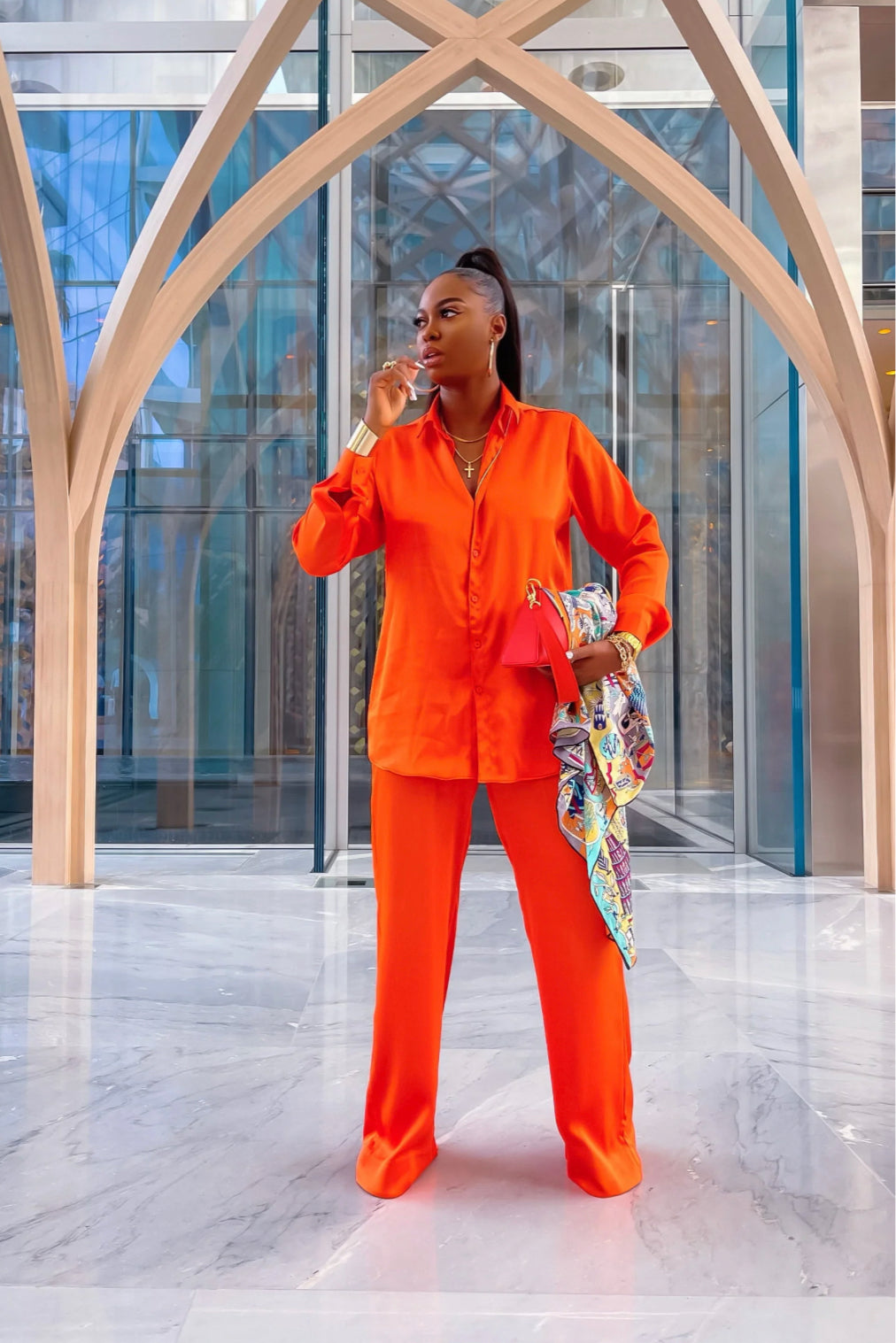 Model wearing Lottie Set in vibrant orange with relaxed long-sleeve button-down shirt and high-waist straight-leg pants, styled with a orange mini bag.