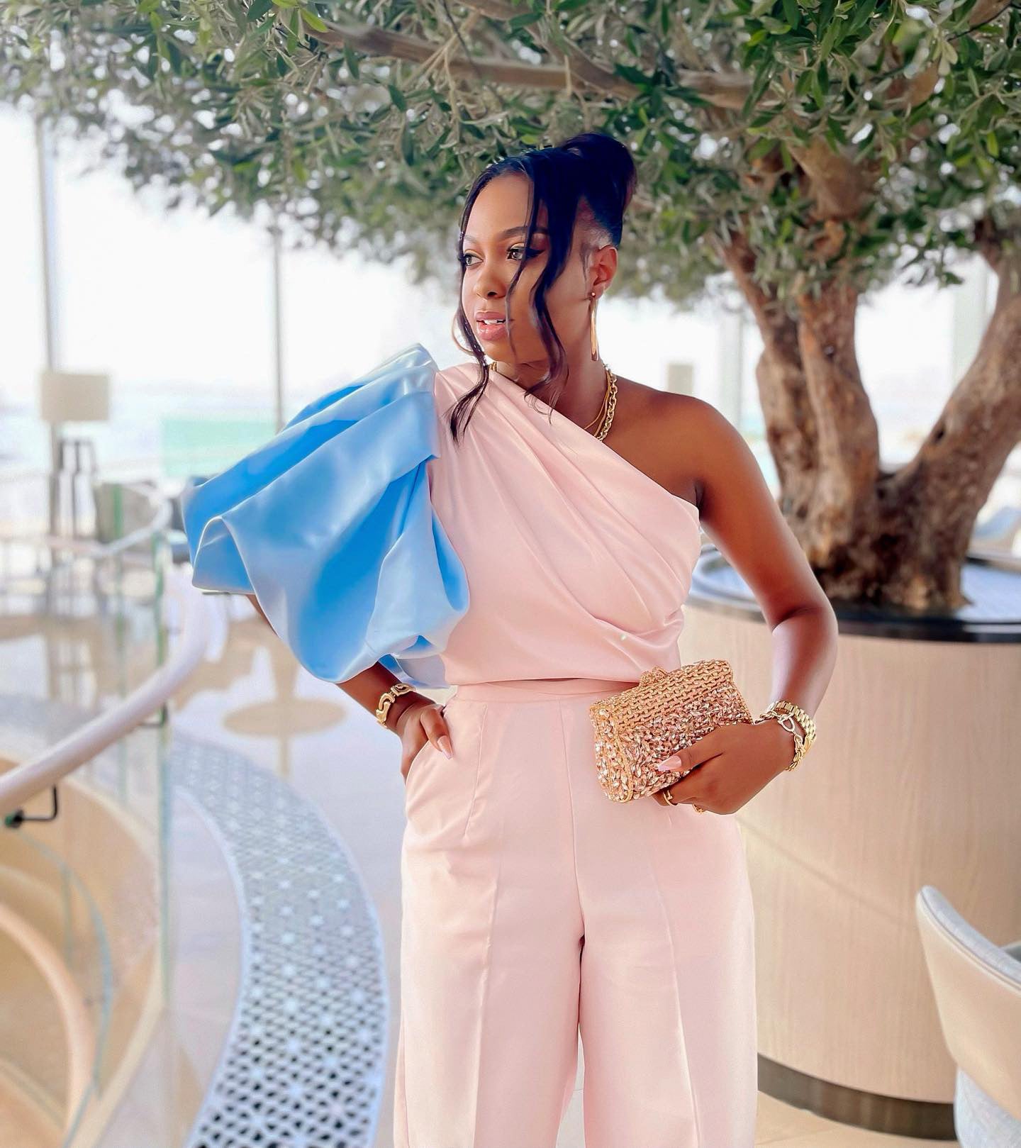 Paris blush pink and sky blue two-piece set with one-shoulder balloon sleeve top and high-waist tailored pants, styled with gold clutch.