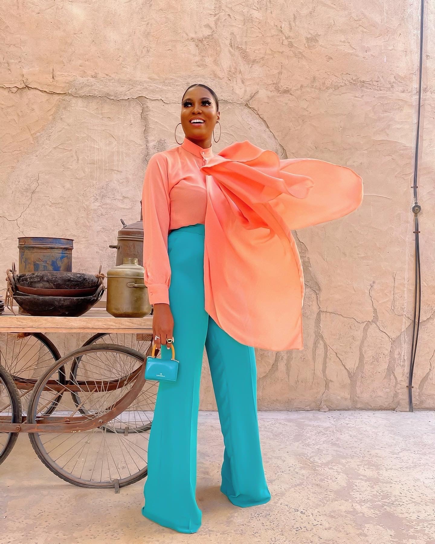 A 5ft 11in model wearing an elegant colour pop coord set featuring a peach coloured blouse and teal green high-waist straight pants.