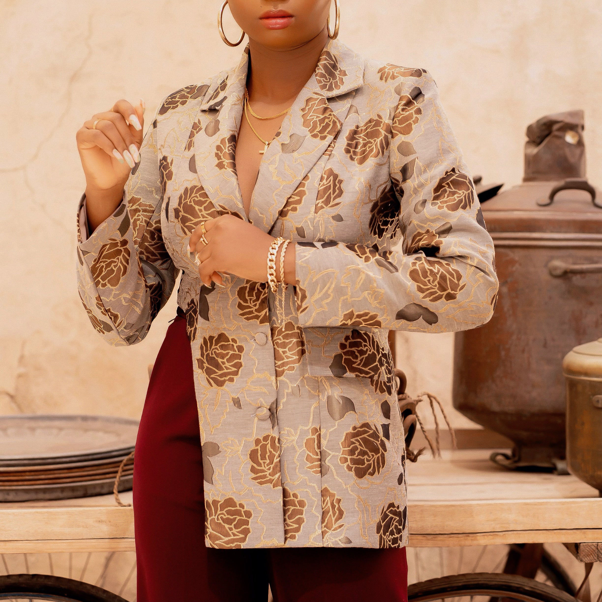 Close-up of a tailored brocade blazer featuring gold floral detailing and sharp lapels, worn over burgundy pants.